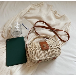 Close-up of beige straw handbag with brown leather flap and golden twist lock detail