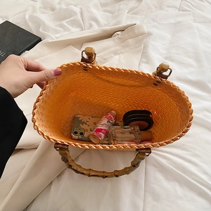 Orange woven handbag with bamboo handle showing large interior capacity on white bedding