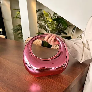 Metallic pink crescent evening bag with acrylic mirror finish and modern cutout handle
