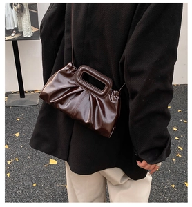 Detail of dark brown pleated handbag with cutout handle and glossy finish on leather