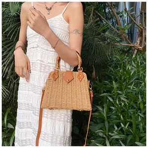 Detail view of woven straw handbag with bamboo handles and adjustable leather strap