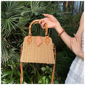 Detail of hand-woven straw bag with bamboo handle and brown leather strap on nature background