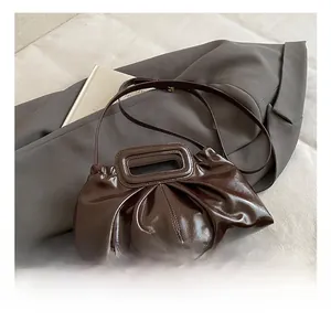 Detail view of deep chocolate brown pleated bag with metallic top handle and smooth finish