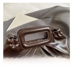Detail of dark brown glossy patent leather handbag with pleated design and sturdy handle