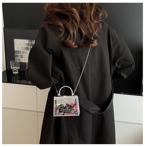 Detailed view of mini floral printed bag with metal chain on a black coat outfit
