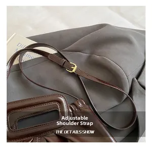 Detail showing an adjustable dark brown leather shoulder strap with golden metal buckle