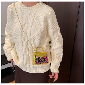 Detail of vintage floral pattern handbag with gold hardware worn on white cable knit sweater