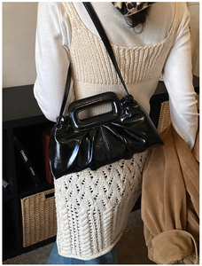 Detail of glossy black pleated shoulder bag with unique rectangular cutout handle and strap