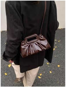 Brown pleated tote bag with glossy finish shown on model wearing a black long coat