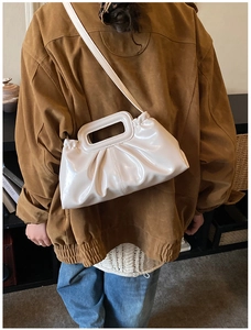 Chic cream ruched crossbody bag with hollow handle shown on model in warm studio setting