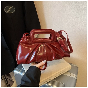 Close-up of deep red patent leather shoulder bag with pleated texture and gold hardware