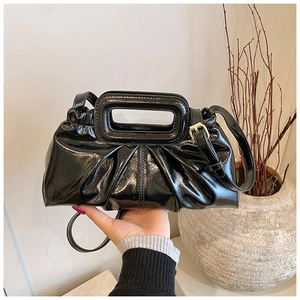 Detail of black glossy pleated shoulder bag with rectangular handle and gold hardware