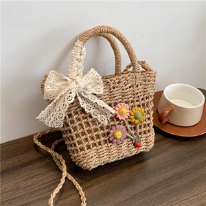 Dettaglio della borsa in paglia intrecciata con fiocco di pizzo, fiori e manici