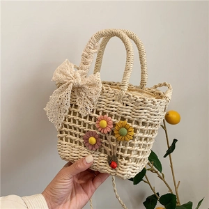 Dettaglio della borsa in paglia con fiori all'uncinetto, fiocco e coccinella