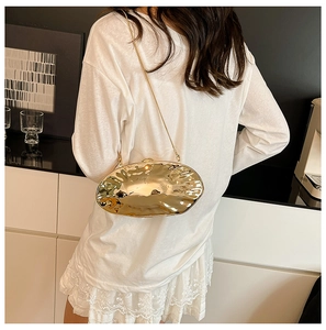 Dettaglio di una borsa da sera asimmetrica dorata con catena sottile su una modella