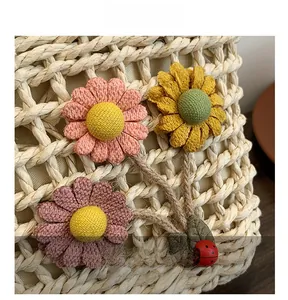 Dettaglio della borsa in paglia fatta a mano con fiori 3D tessuti e ciondolo a coccinella