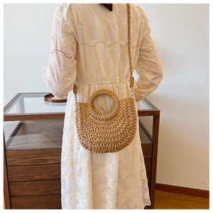 Détail d'un sac en paille demi-lune avec poignée ronde évidée et bandoulière tissée