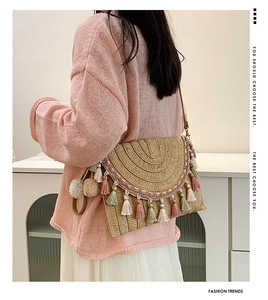 Detail of straw woven crossbody bag with colorful tassels on a beige bohemian envelope bag