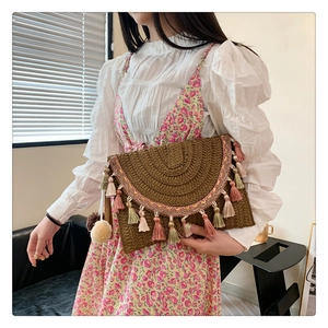 Detail of bohemian straw clutch with colorful tassels and ethnic floral embroidery