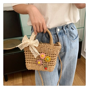 Dettaglio borsa in paglia intrecciata con fiori colorati e fiocco di pizzo bianco