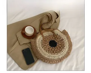 Detailed top view of a round woven straw beach bag with brown leather straps on a bed