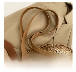 Close-up of leather straps and cross-stitch detailing on round woven straw shoulder bag