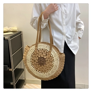 Close-up of a large round woven straw tote bag with brown leather straps for summer beach