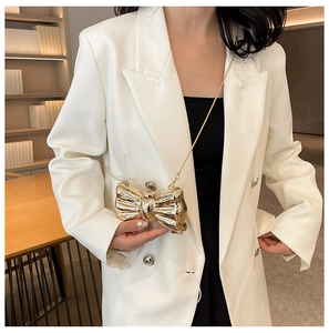 Detail of a mini gold bow clutch with metallic mirror finish and golden chain strap