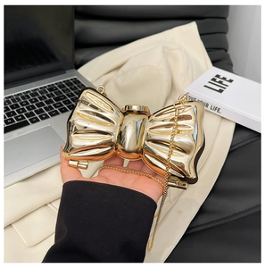 Close-up of elegant gold bow-shaped evening bag with metallic mirror finish and fine chain