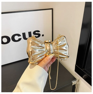 Detail of a mini bow-shaped acrylic evening bag with mirror metallic finish and gold chain