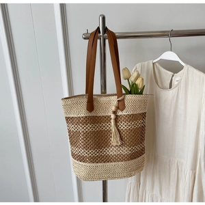 Détail d'un sac de plage en paille tissée avec anses en cuir marron et pompon décoratif chic