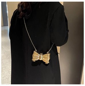 Golden bow-shaped evening clutch bag with chain strap worn on a black blazer jacket