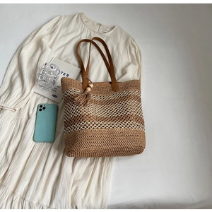 Détail d'un sac cabas en paille tissée avec rayures et breloque à pompon en cuir