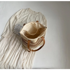 Détail du sac en paille à carreaux avec lanières en cuir et décoration à pompon