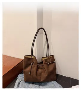 Detailed view of brown faux suede tote with side drawstrings and silver beads on denim