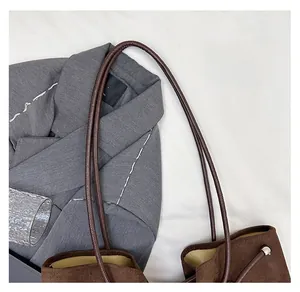 Detail of brown suede tote bag with cylindrical handles and metallic rivet accents