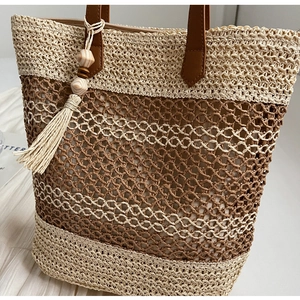 Détail du sac cabas en paille tressée avec anses en cuir brun et pompon déco