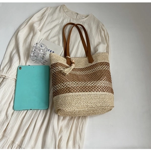 Détail d'un sac cabas en paille tissée avec pompons marrons et texture maillée sur robe blanche