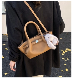 Detail of brown leather bucket bag with metal buckle and plush bunny charm accessory