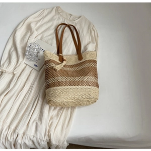 Détail d'un sac cabas en paille tissée avec anses en cuir marron et pompon en bois