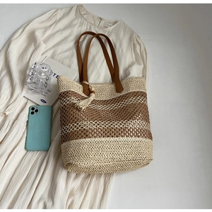 Vue à plat d'un sac cabas en paille rayé avec lanières en cuir et pompon sur robe