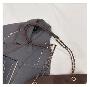 Detail of brown faux leather handbag with gold metal chain strap on gray blazer background