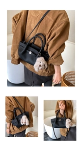 Detail of black pebbled leather tote bag with silver clasp and grey plush bunny charm