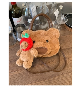Close-up of brown plush bear bag with strawberry bear pendant on wooden table