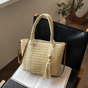 Stijlvolle beige strooien draagtas met lederen riem en kwast op een lederen stoel
