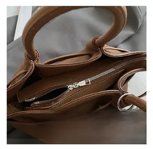 Close-up of brown pebbled leather handbag with silver zipper and grey faux fur pompom charm
