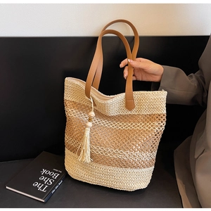 Gros plan du sac de plage tressé avec poignées en cuir marron et pompons en bois