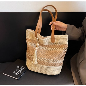 Détail du sac cabas en paille tressée avec poignées en cuir marron et pompon à perles