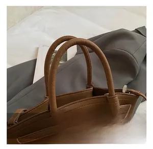 Close-up of brown pebbled leather handbag with decorative straps and plush charm
