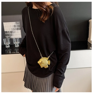 Dettaglio di una borsa da sera dorata a forma di pesce con trama a squame e catena
